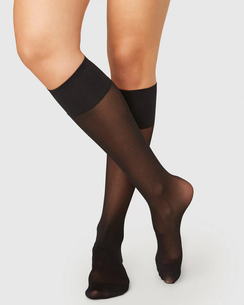 Black knee-high socks worn by a person on a light gray background