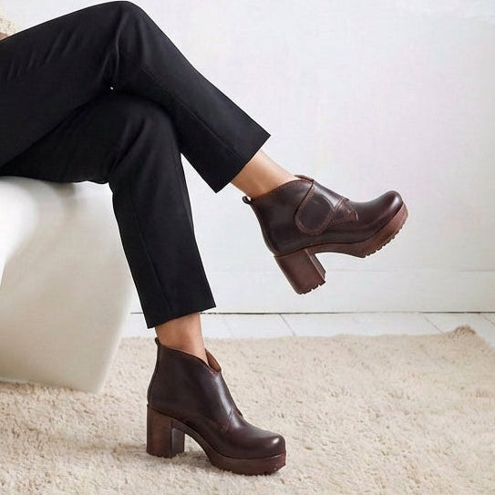 Person wearing brown leather boots and black pants sitting on a white chair.