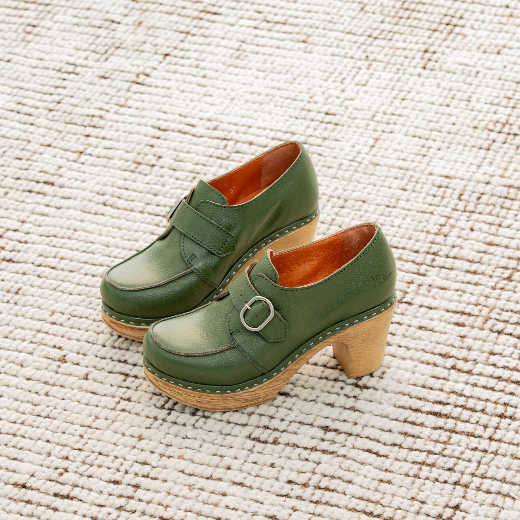 Green clogs with wooden soles on a textured beige surface