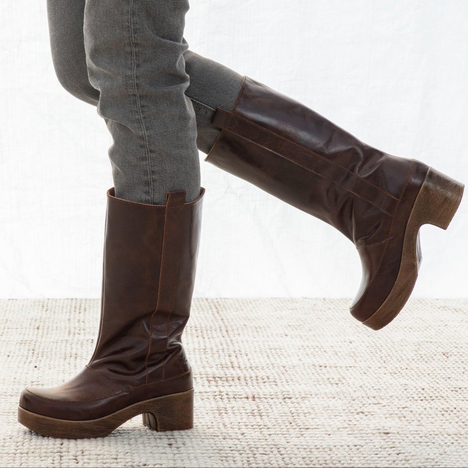 Brown knee-high boots worn with gray jeans on a light background