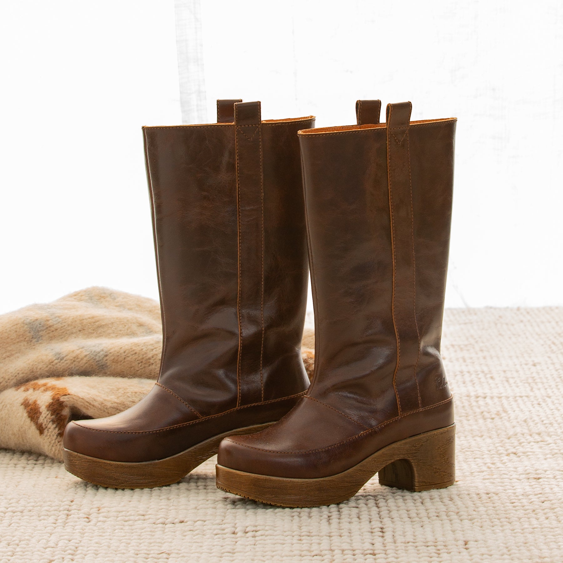 Pair of brown knee-high leather boots on a textured surface with a light background