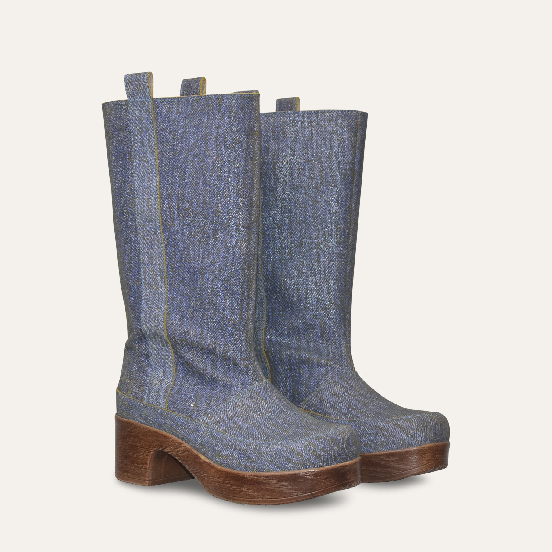 Pair of blue denim knee-high boots with brown soles on a light gray background