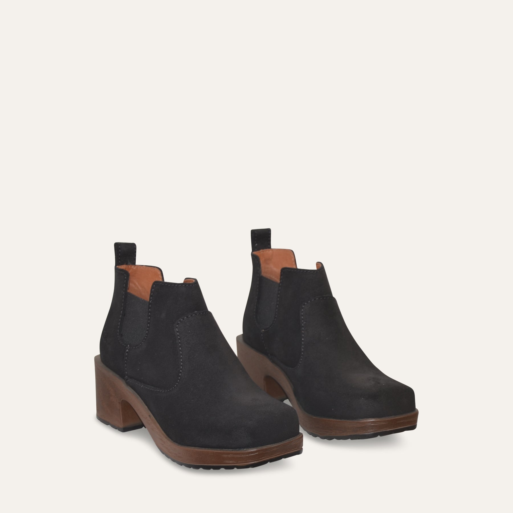 Pair of black ankle Chelsea boots with brown soles on a light gray background