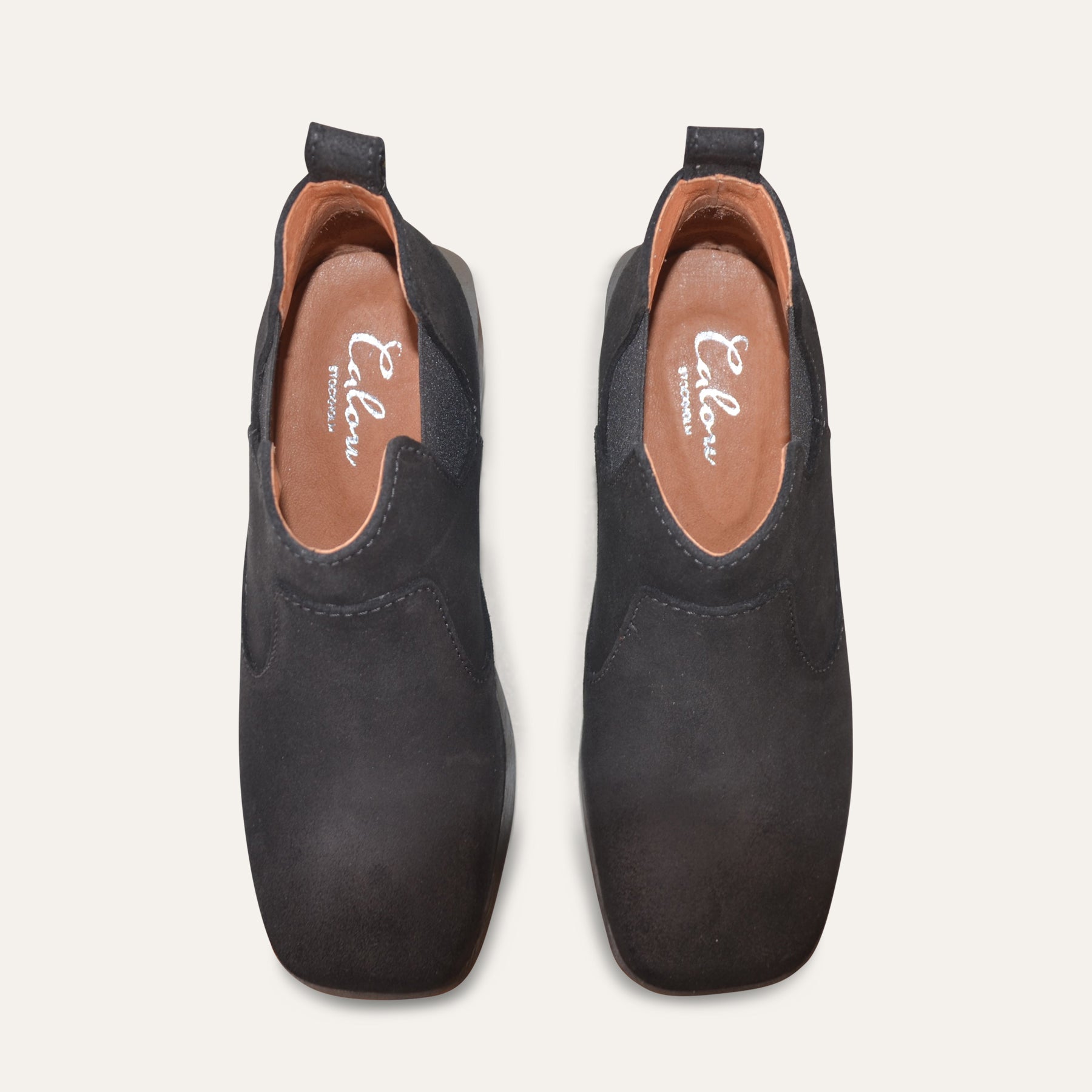 Pair of black ankle clog boots with brown soles on a white background, top view