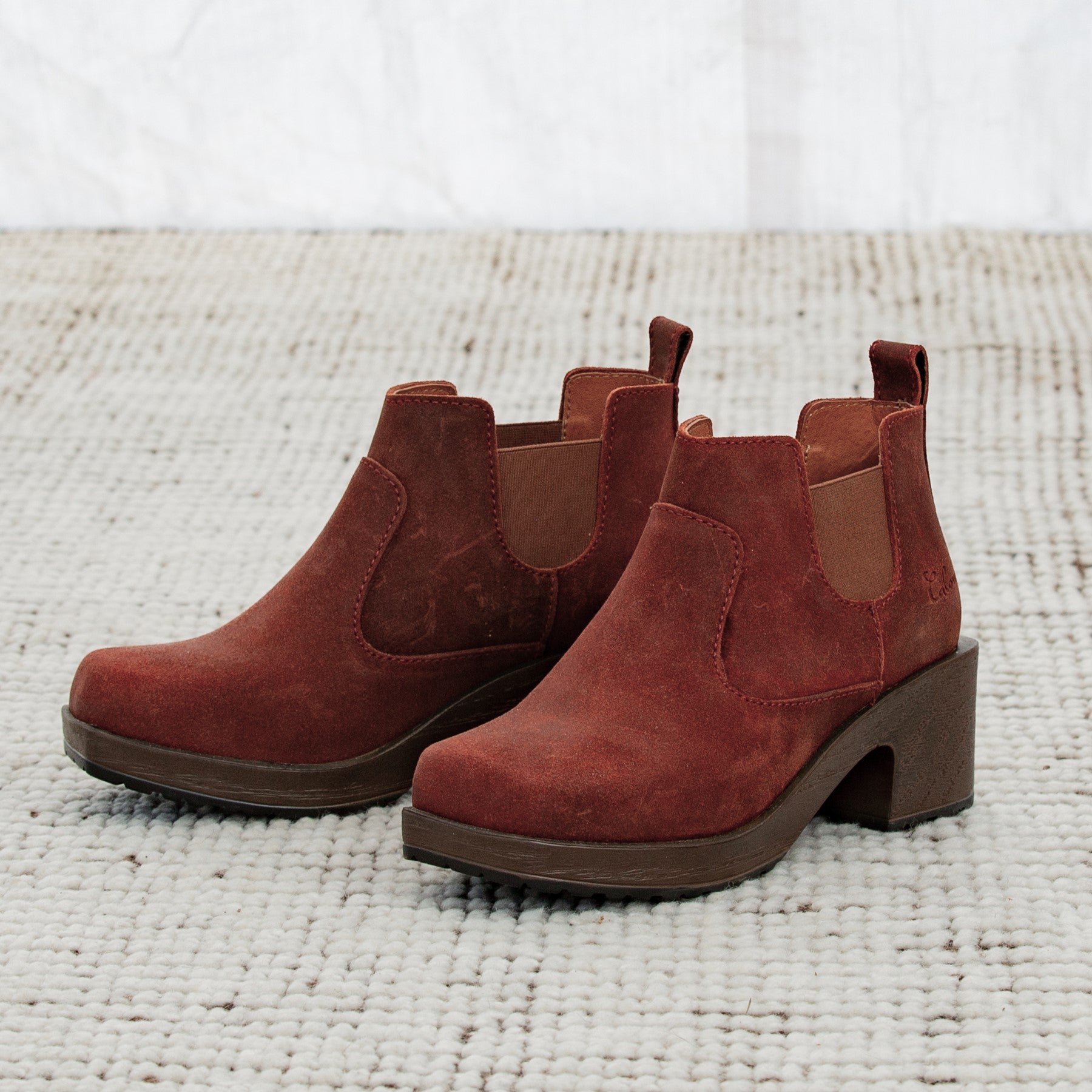 Pair of red suede ankle boots on a textured white surface