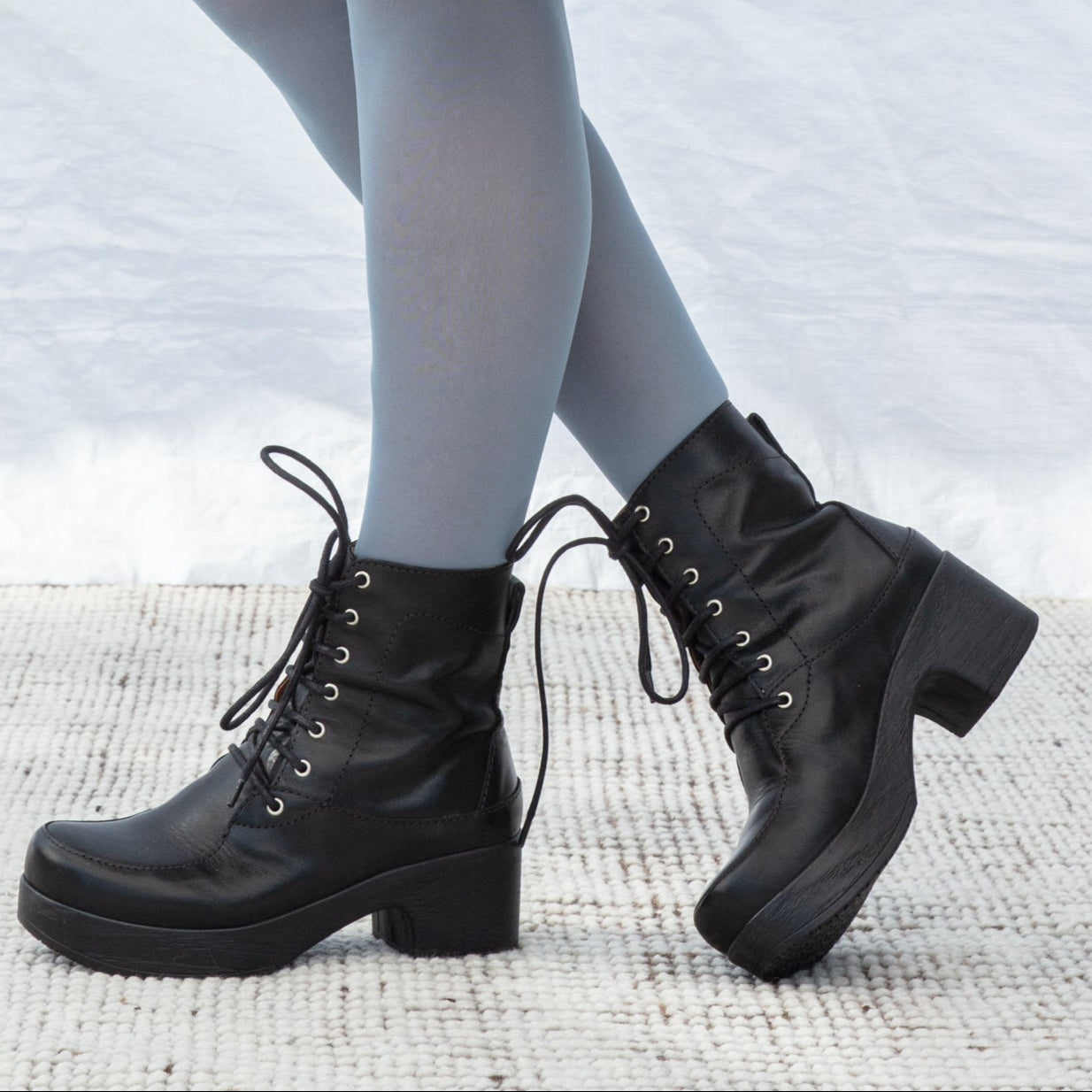 Person wearing black lace-up boots with a neutral background