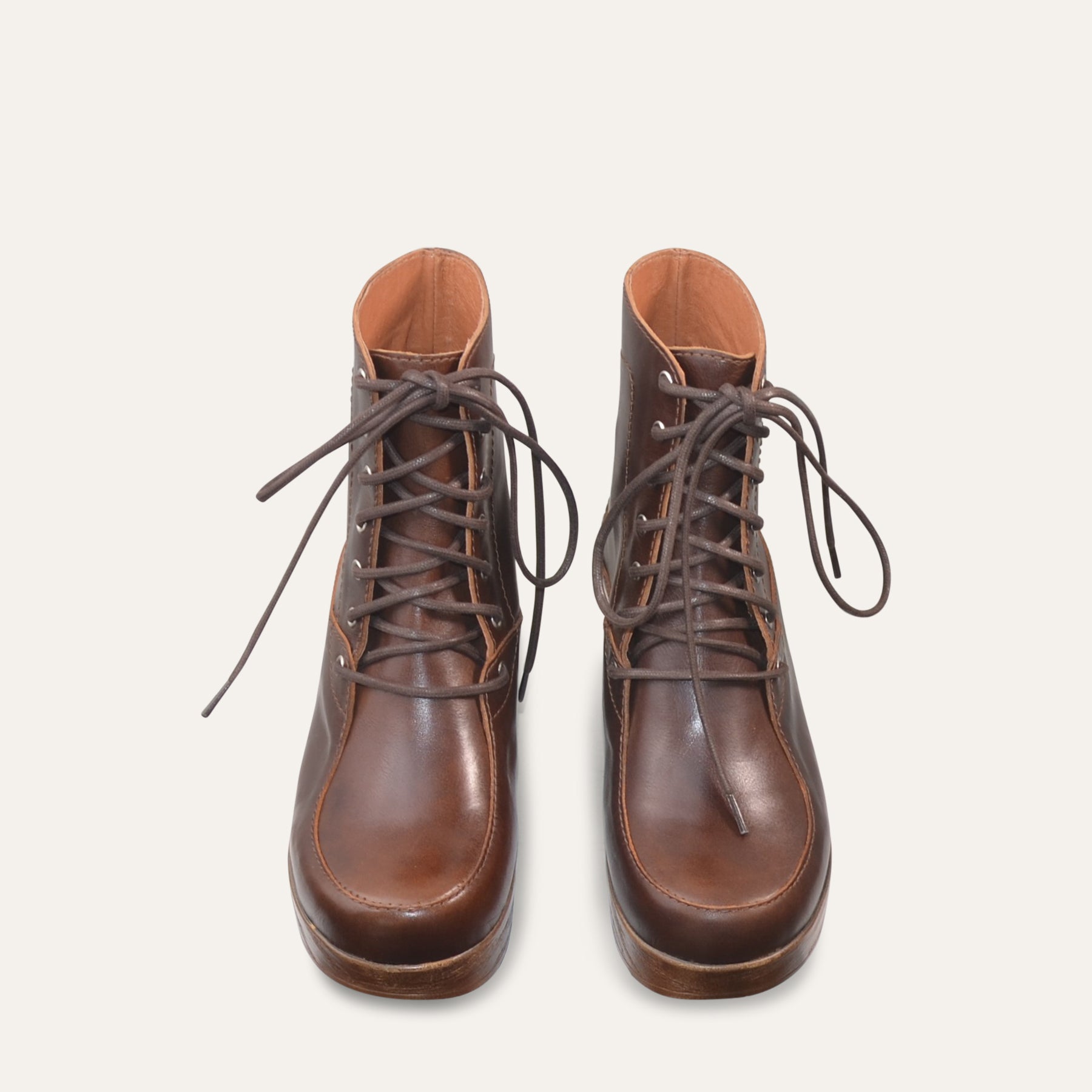 Pair of brown leather boots with laces on a light gray background