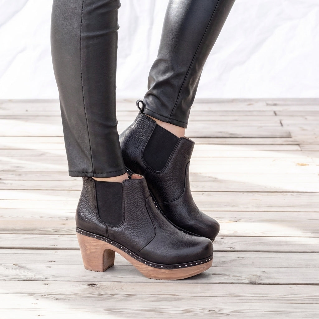 A pair of women's black leather ankle boots with elastic side panels and light brown wood-look block heels, soft, flexible and shockabsorbing.