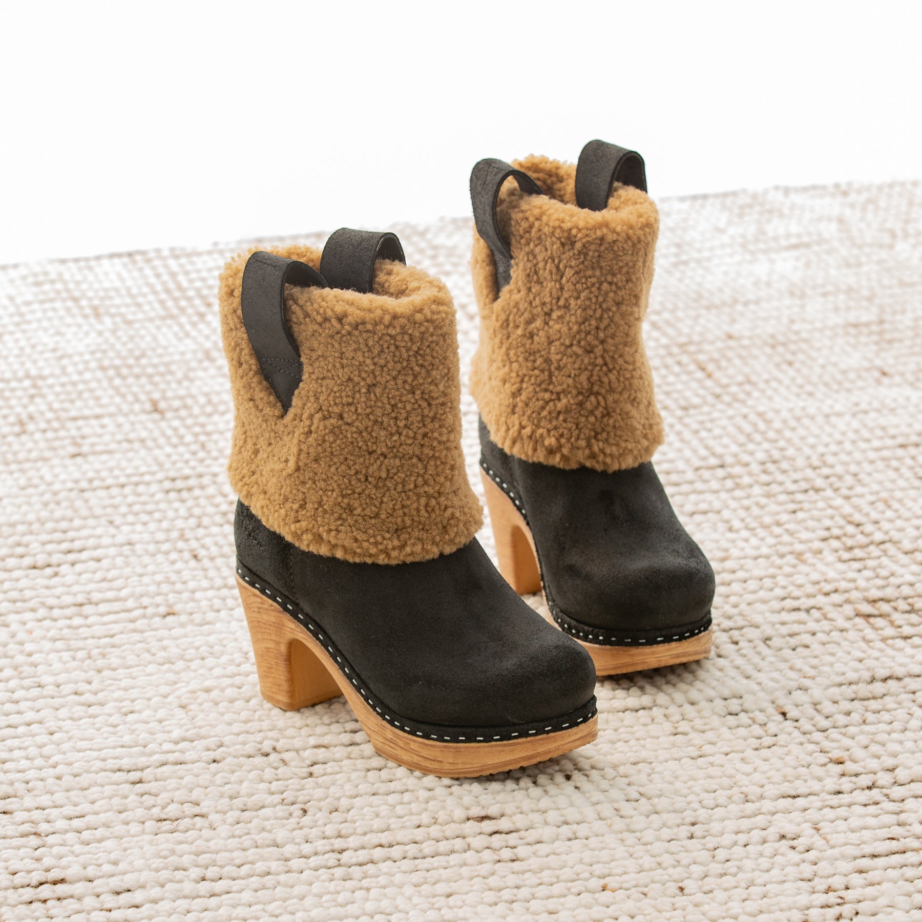 Pair of black and brown boots with shearling collar on a textured surface