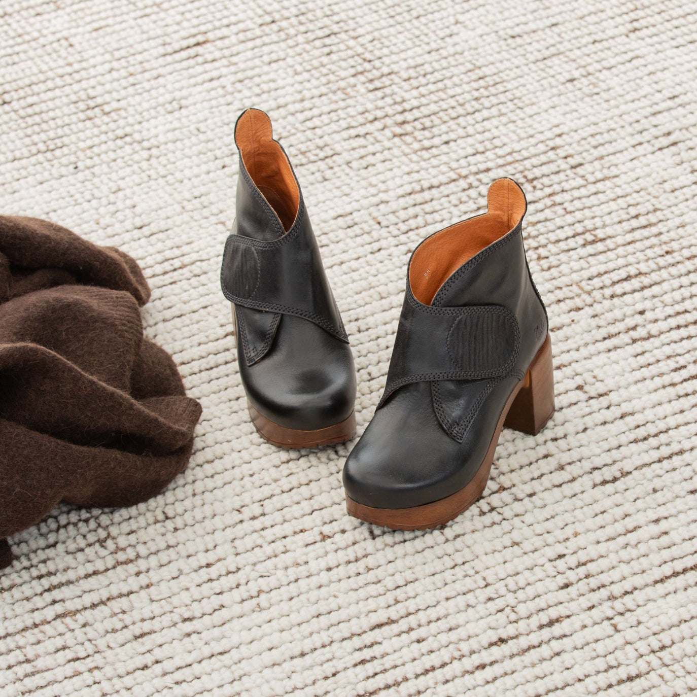 Pair of black leather boots with brown soles on a textured beige surface