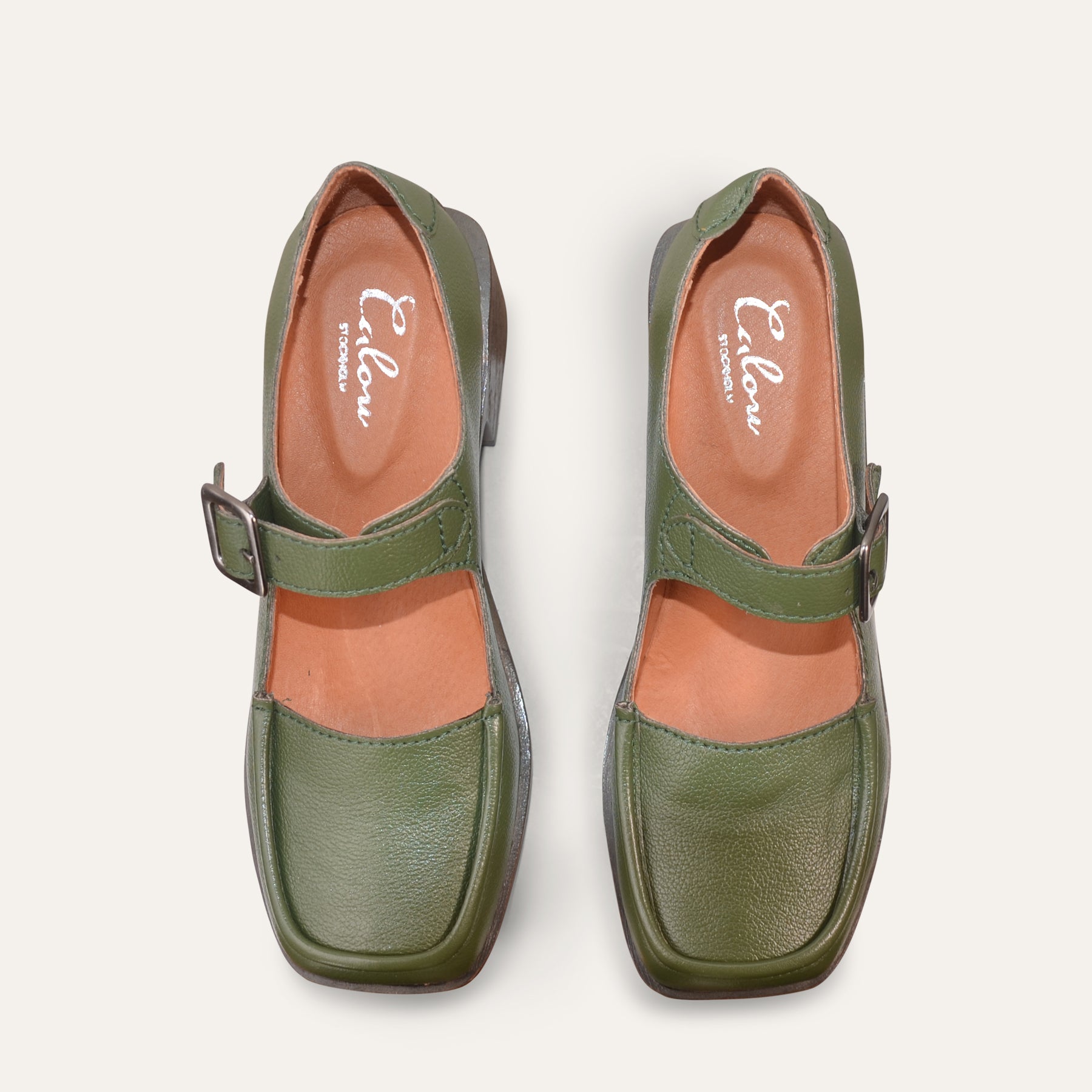 Pair of green Mary-Jane shoes with a strap on a white background