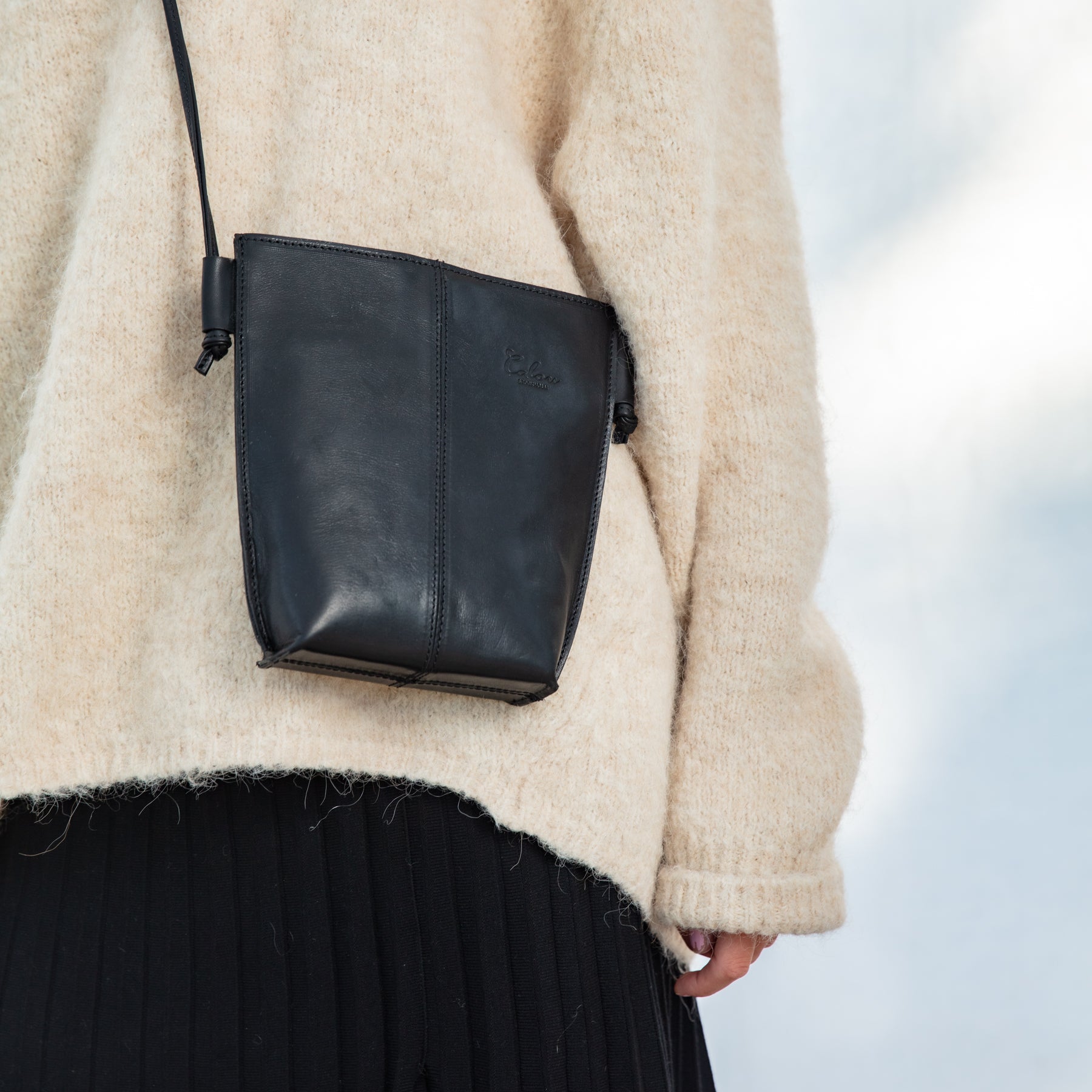 Person wearing a beige sweater and holding a black leather bag against a blurred background