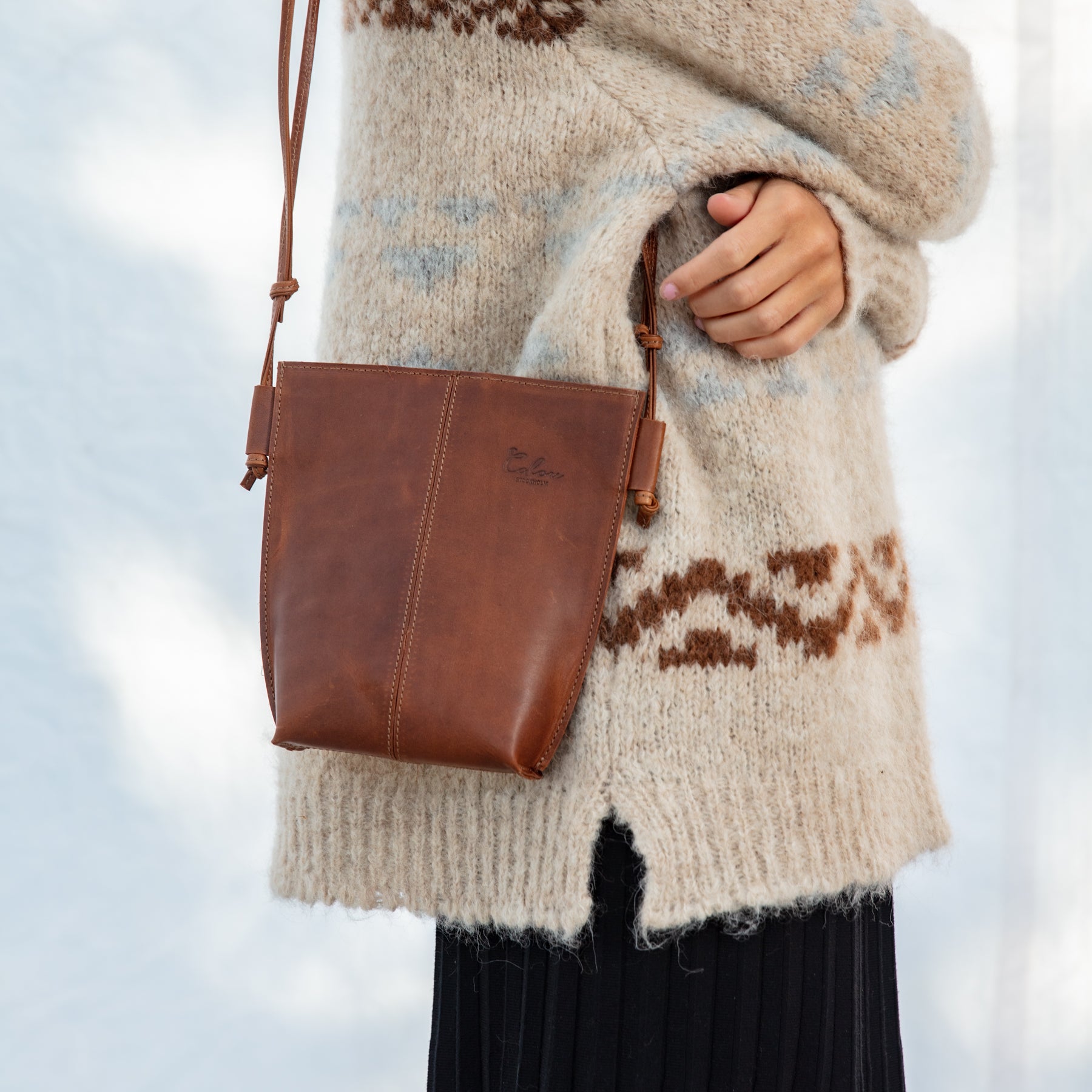 Person wearing a beige sweater with a brown leather crossbody bag against a blurred background