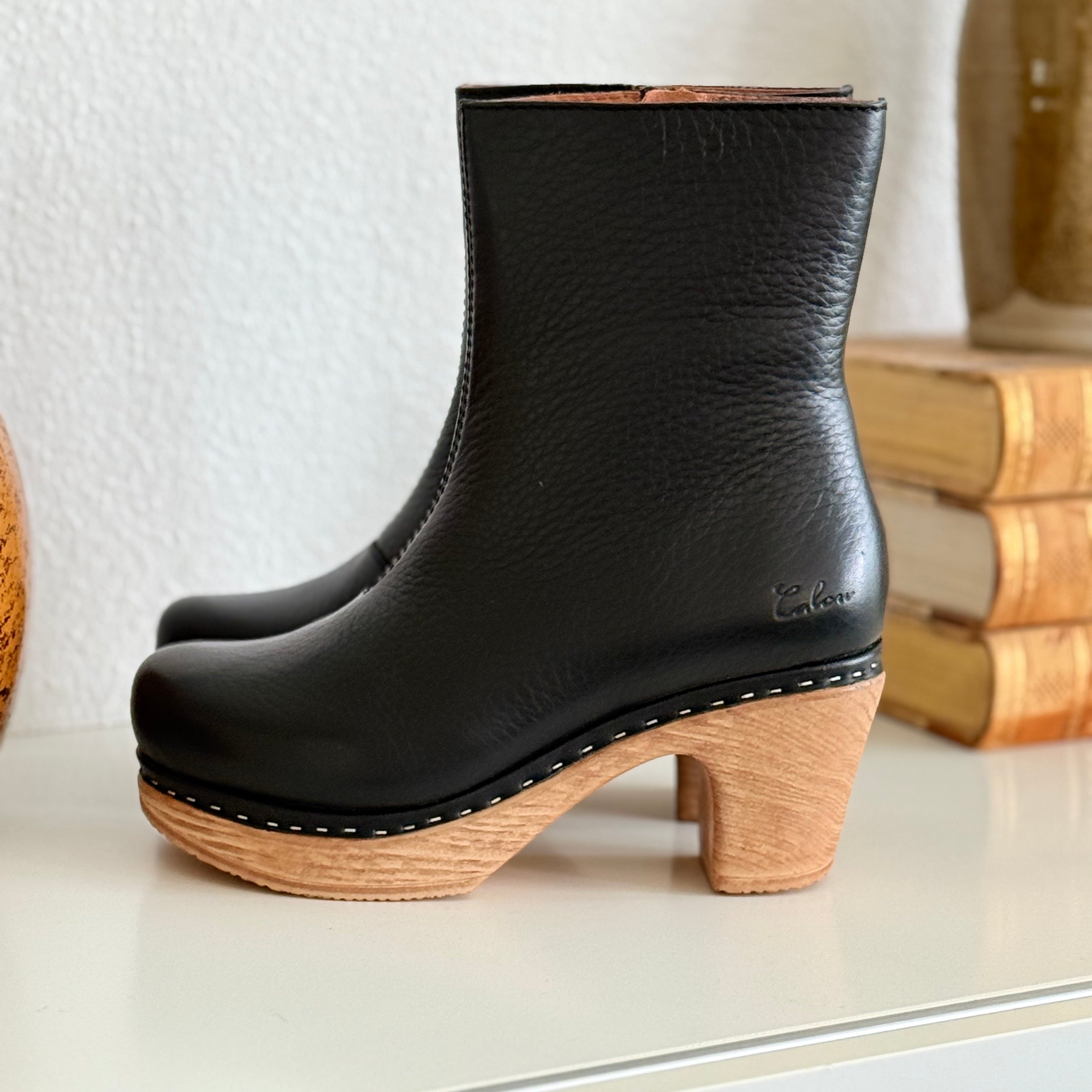 Black clog boots with faux wooden soles on a white surface