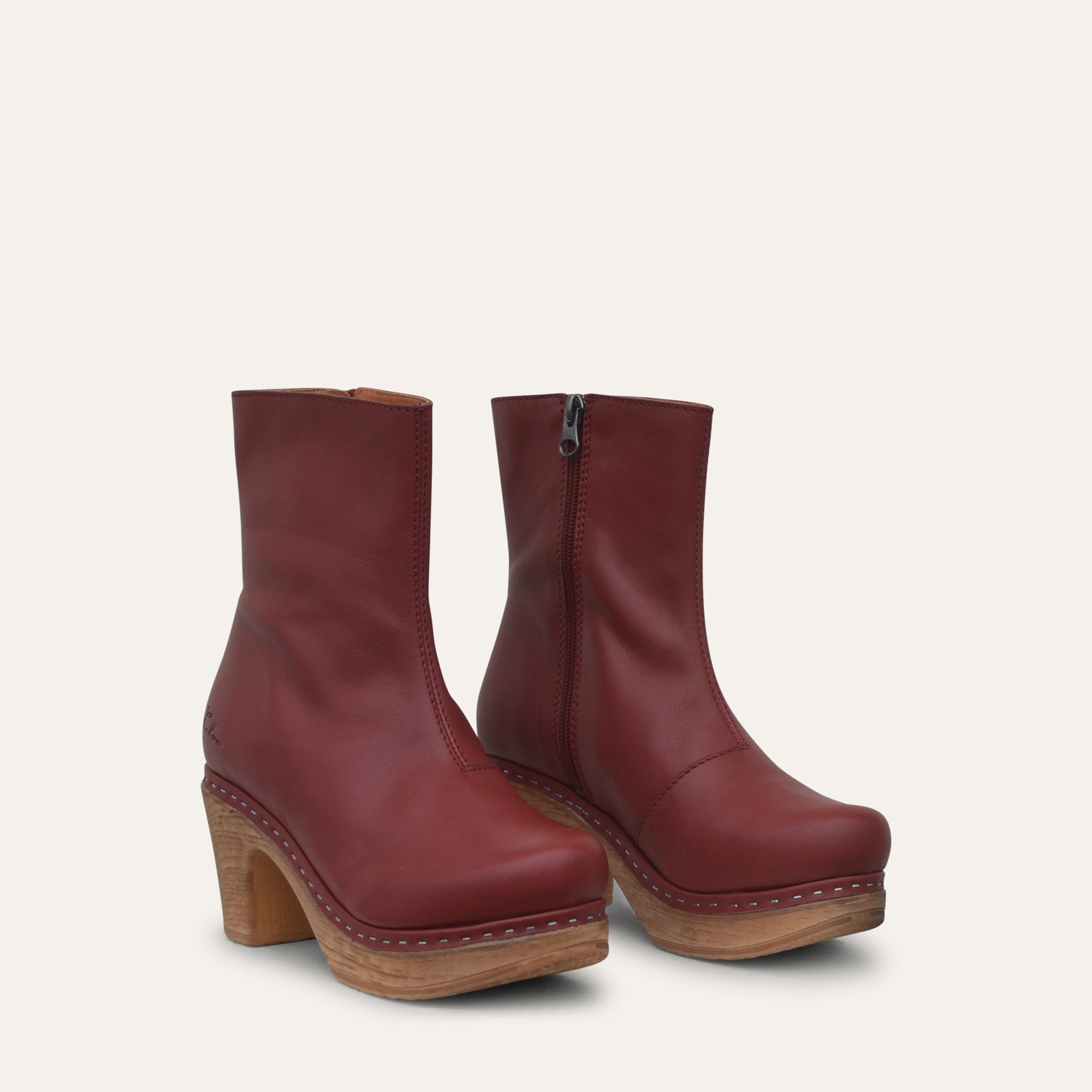 Pair of maroon ankle boots with wooden soles on a light gray background