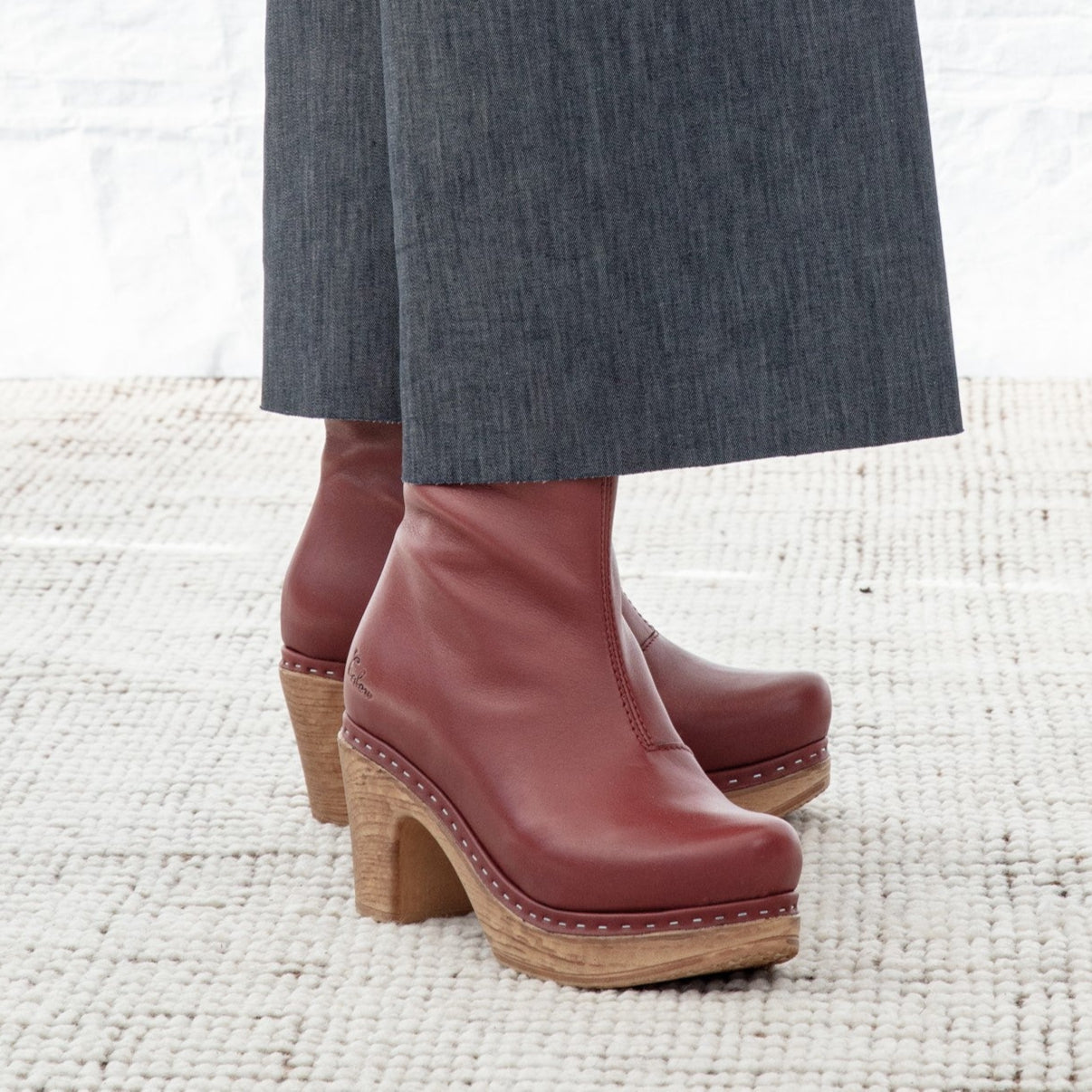 Red clog boots worn with denim pants on a textured white floor.