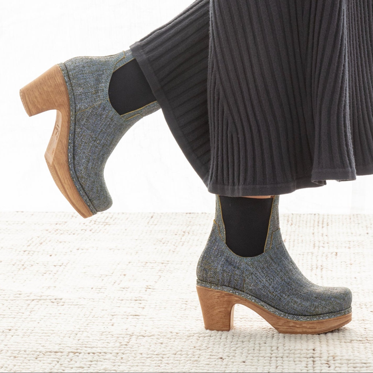 Blue clog shoes with faux wooden soles worn with a black ribbed skirt on a white background