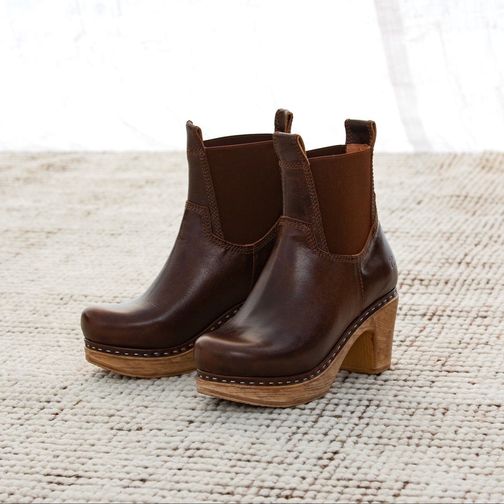 Pair of brown leather boots with wooden soles on a textured surface