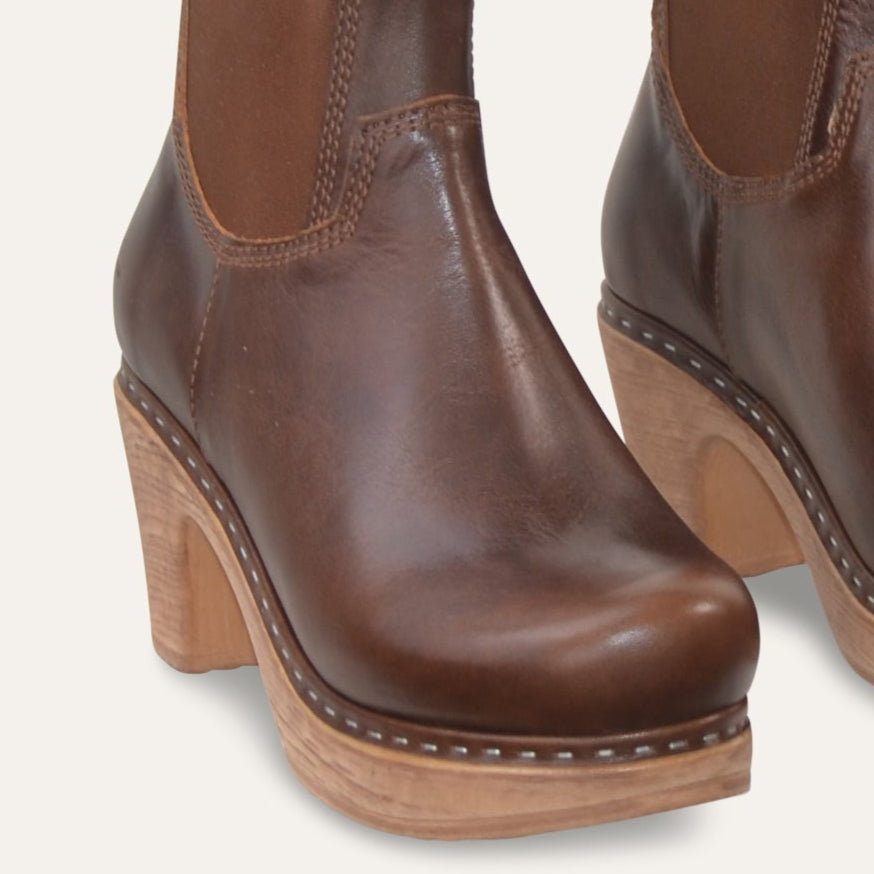Pair of brown leather ankle boots with wooden soles on a light gray background