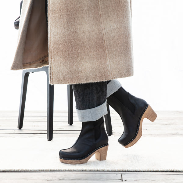 High Black Clog Boot with slim elasticated shaft paired with black jeans and beige coat