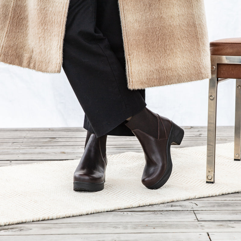 Brown leather ancle clog boot paired with black pants and beige coat 