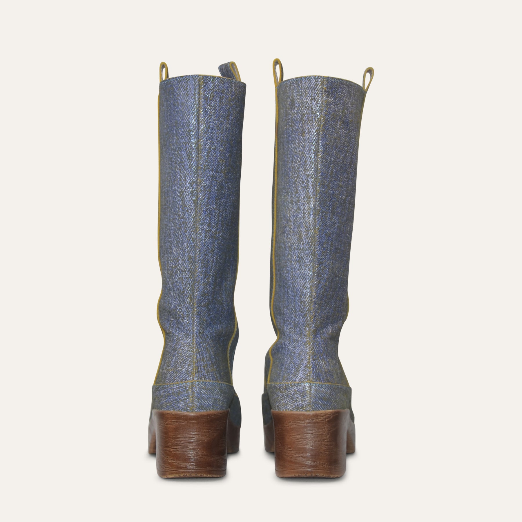 Pair of denim knee-high boots with brown soles on a light gray background