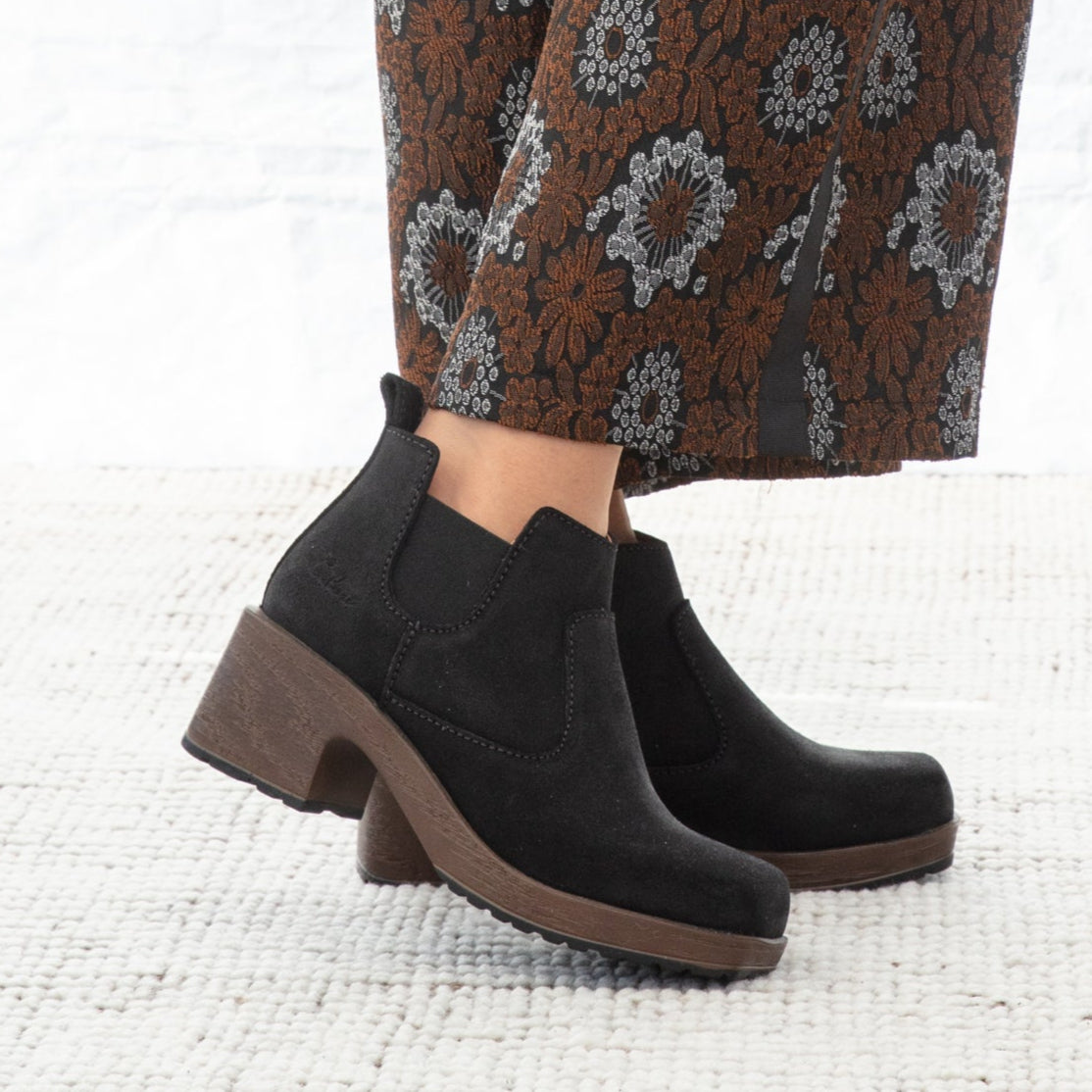 Black boots worn with patterned brown pants on a white background