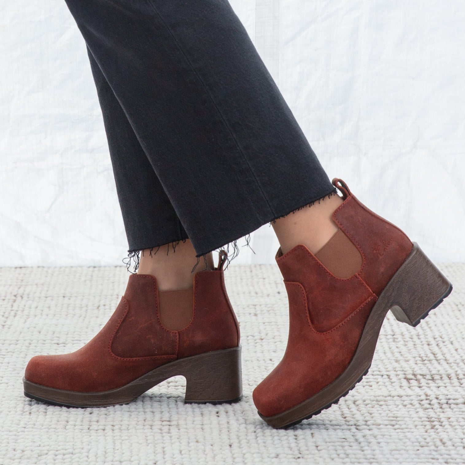 Red ankle boots worn with dark jeans on a textured white surface