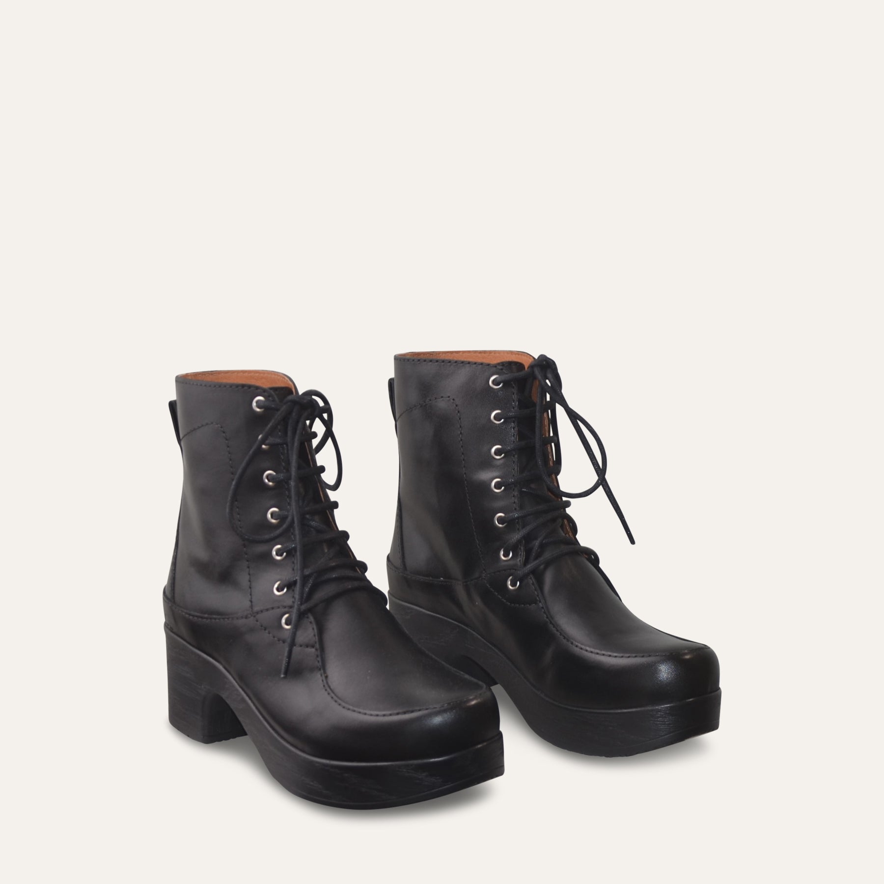 Pair of black leather lace-up boots with black soles on a light gray background