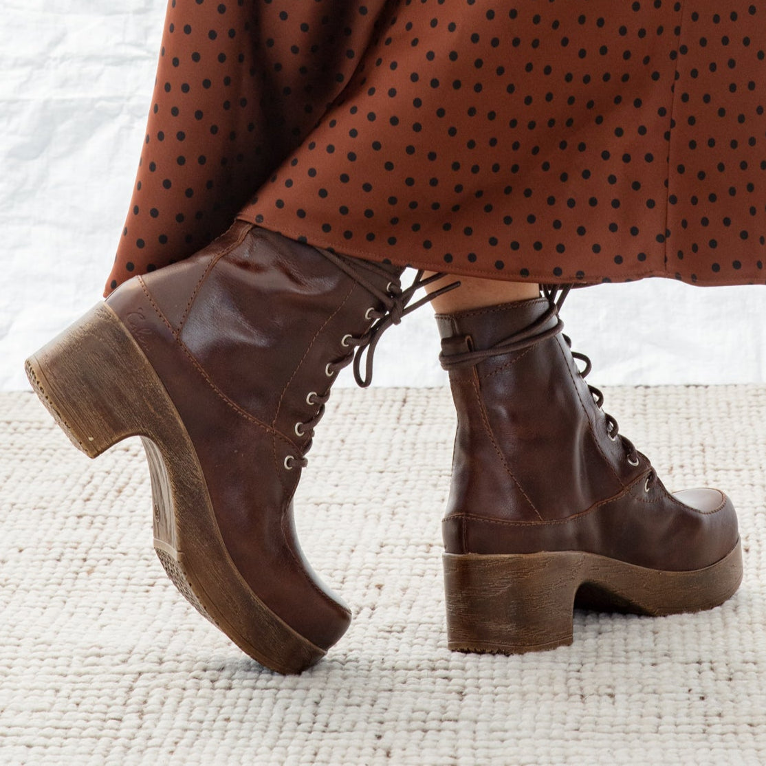 Brown polka dot skirt and brown lace-up boots on a textured white surface