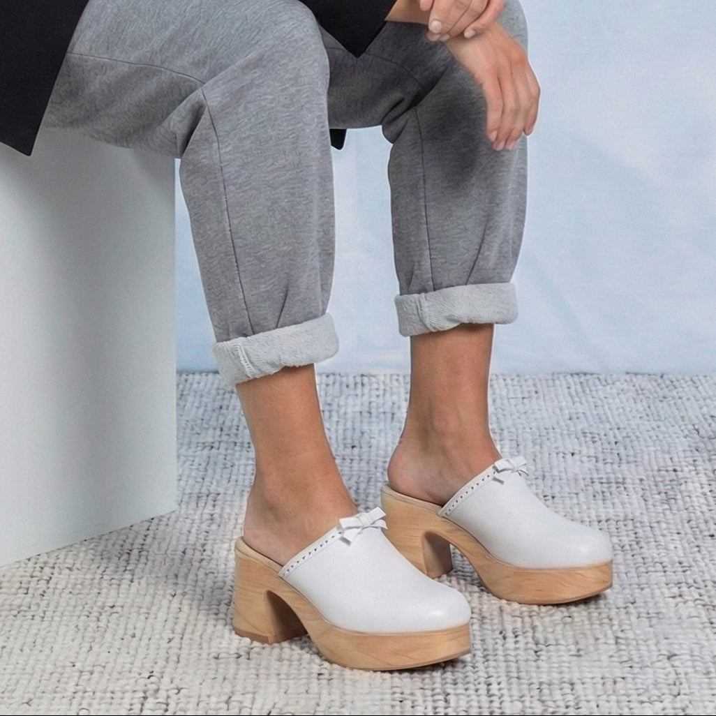 Calou Carla White leather flex-sole clogs worn by a person sitting on a textured surface.