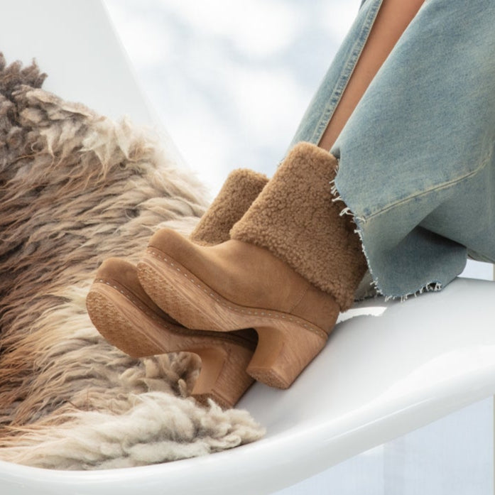 Brown fuzzy boots worn with light blue jeans on a white surface.