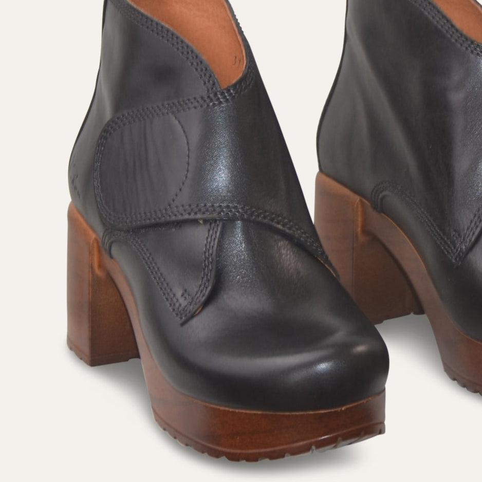 Pair of black leather ankle boots with brown soles on a light gray background
