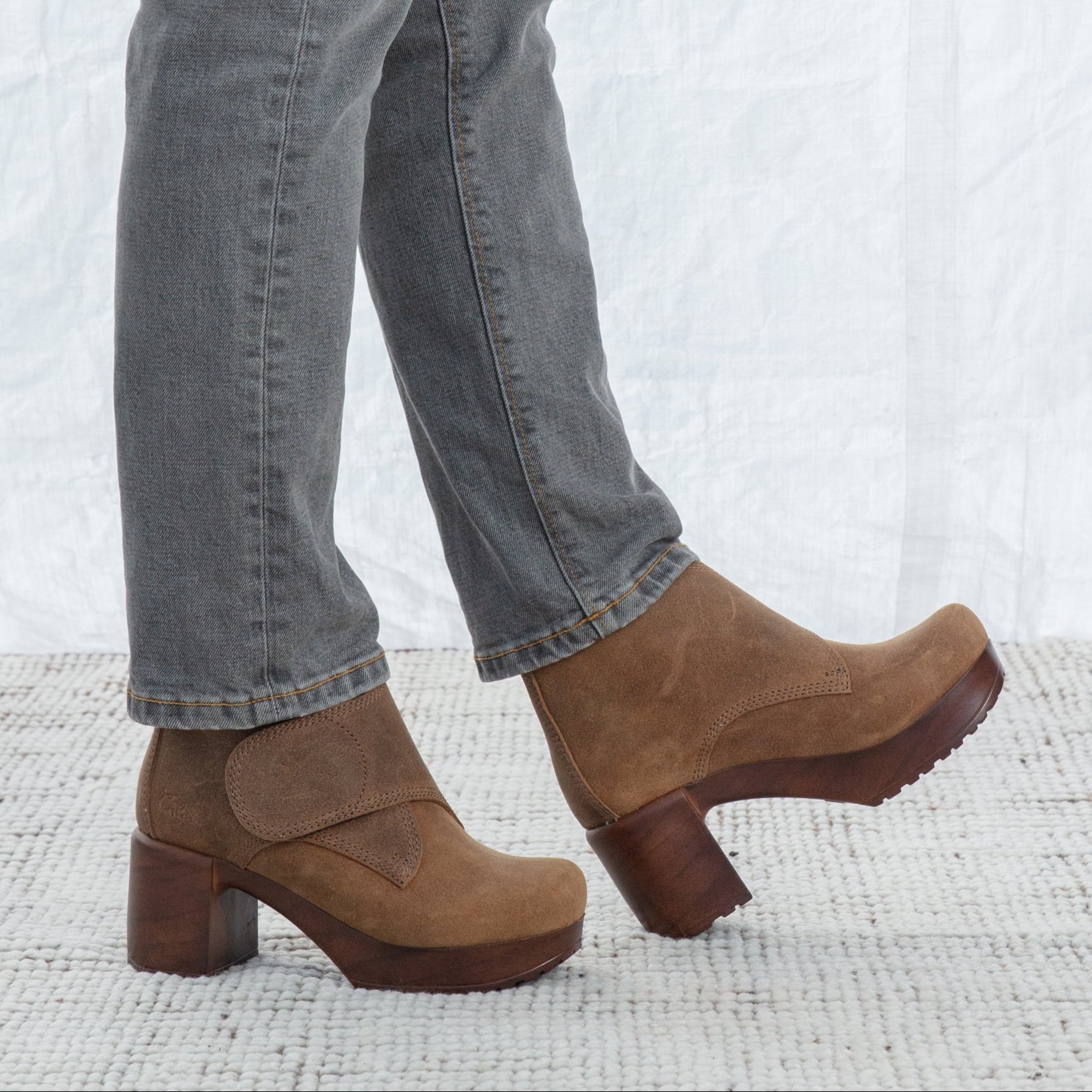Camel clogs worn with gray jeans on a textured white surface
