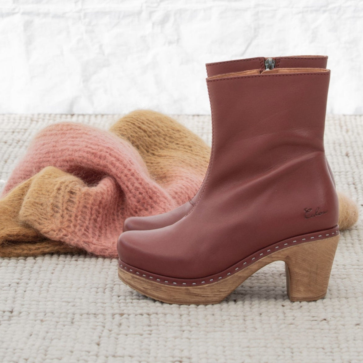 Brown leather boot with wood-like sole on a textured surface with knitted items.