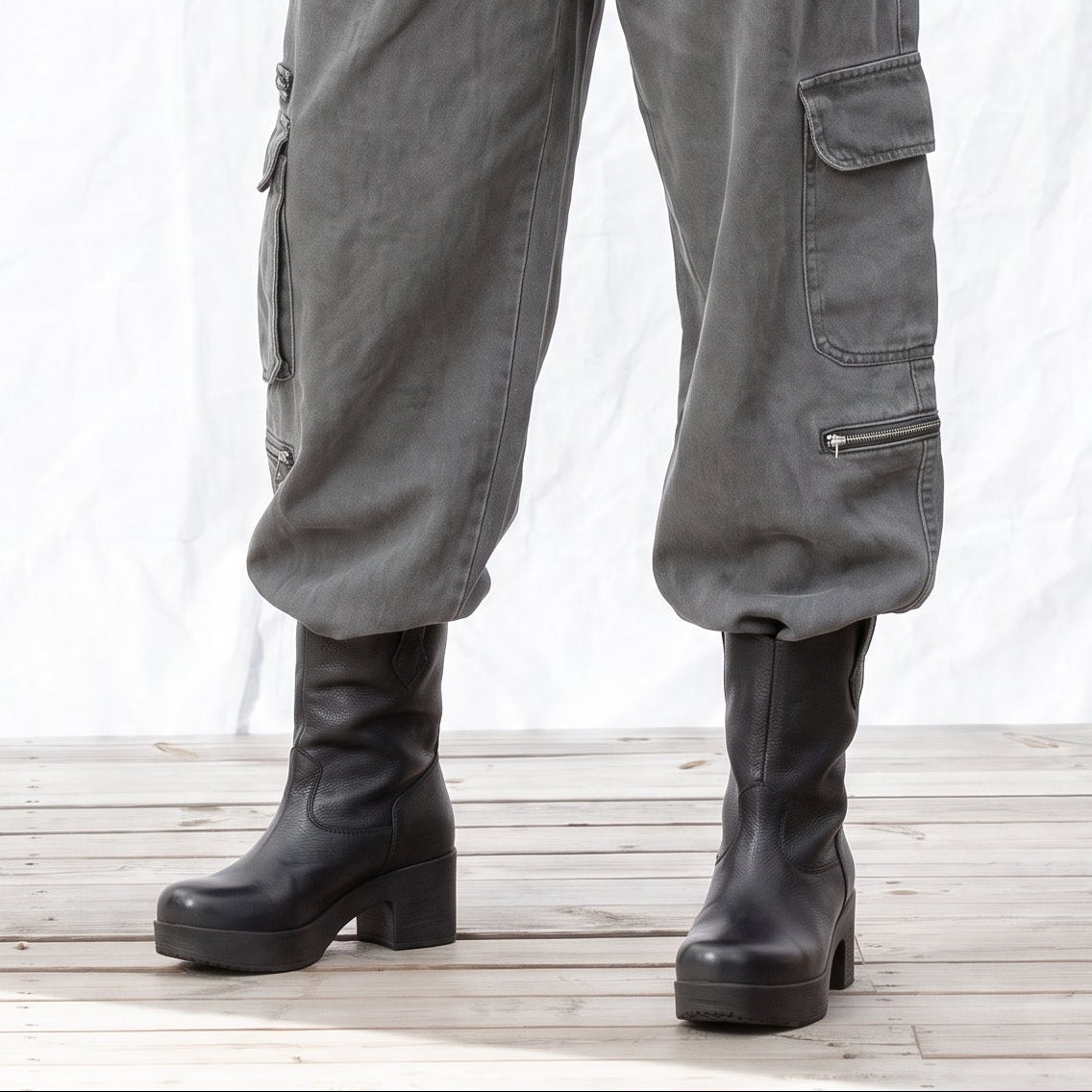 A person wearing high-waisted gray cargo pants with pleated detailing, paired with black ankle boots set on Calou soft, flexible soles. 