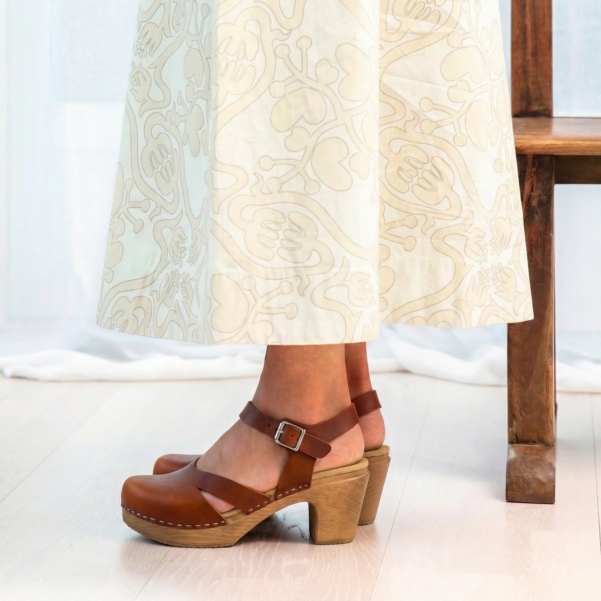 Calou Brown Mary Jane clogs on flexible soles worn with a white dress on a light wooden floor.