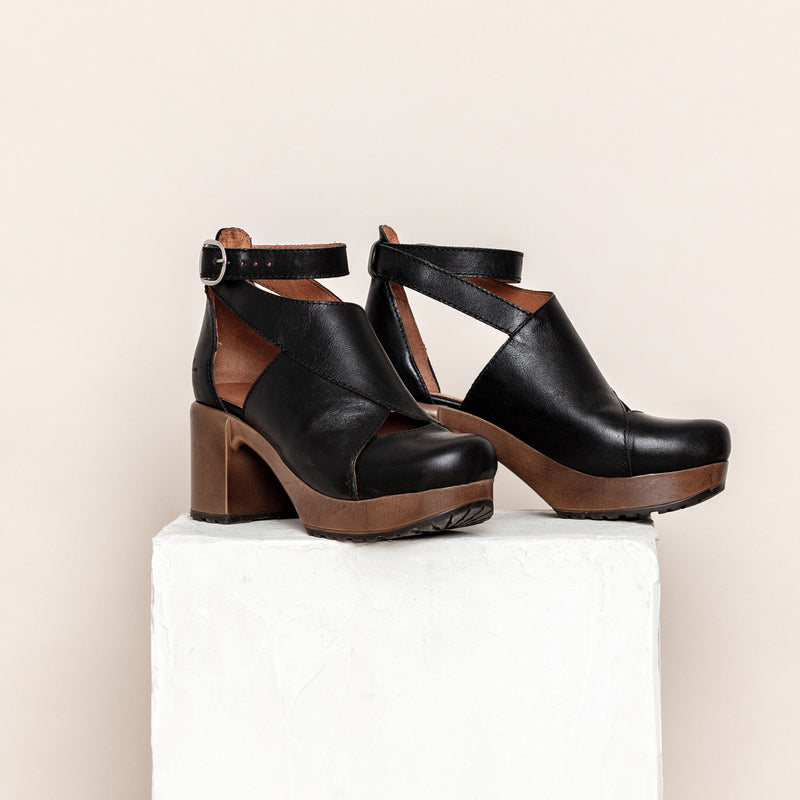 pair of black leather high clog shoes on plinth